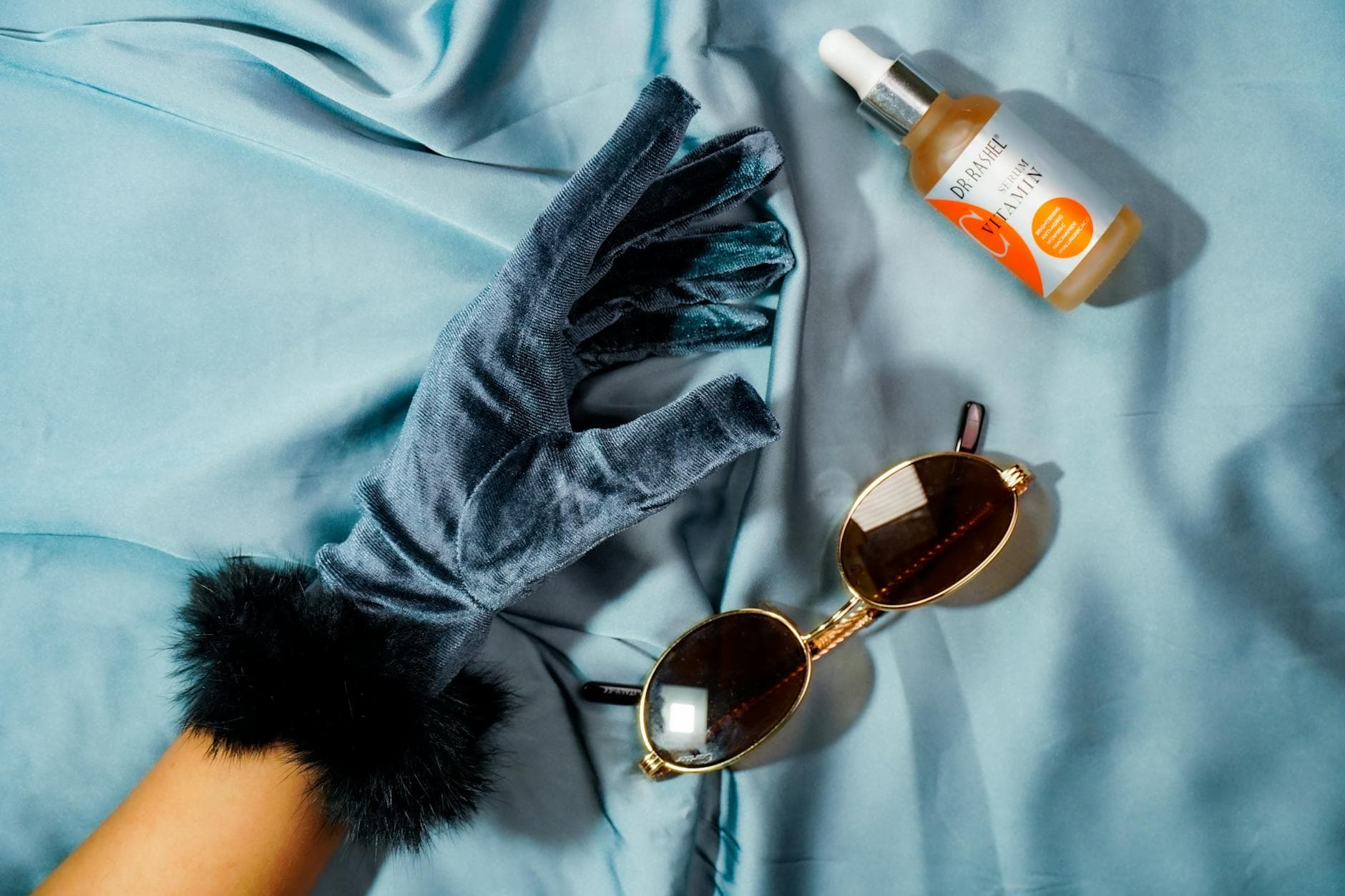 Winter skincare products with gloves and sunglasses on blue fabric